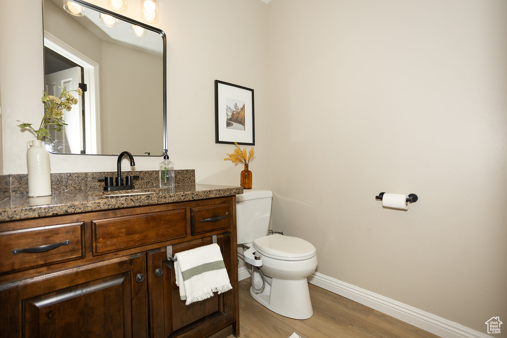 Half bath featuring baseboards, toilet, wood finished floors, and vanity