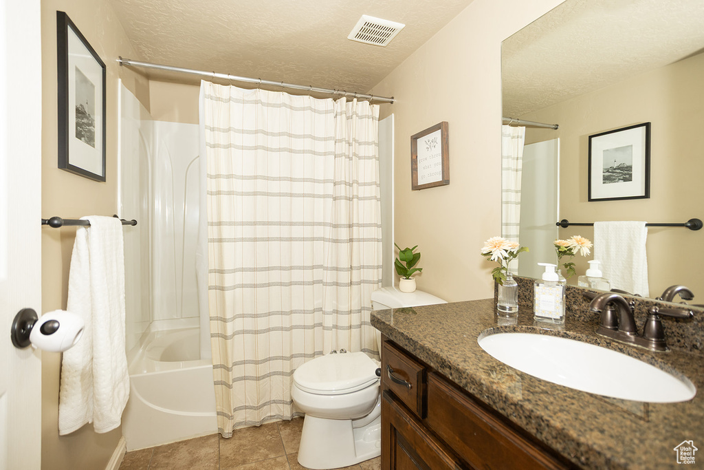 Bathroom featuring toilet, tile patterned flooring, vanity, shower / bathtub combination with curtain, and a textured ceiling