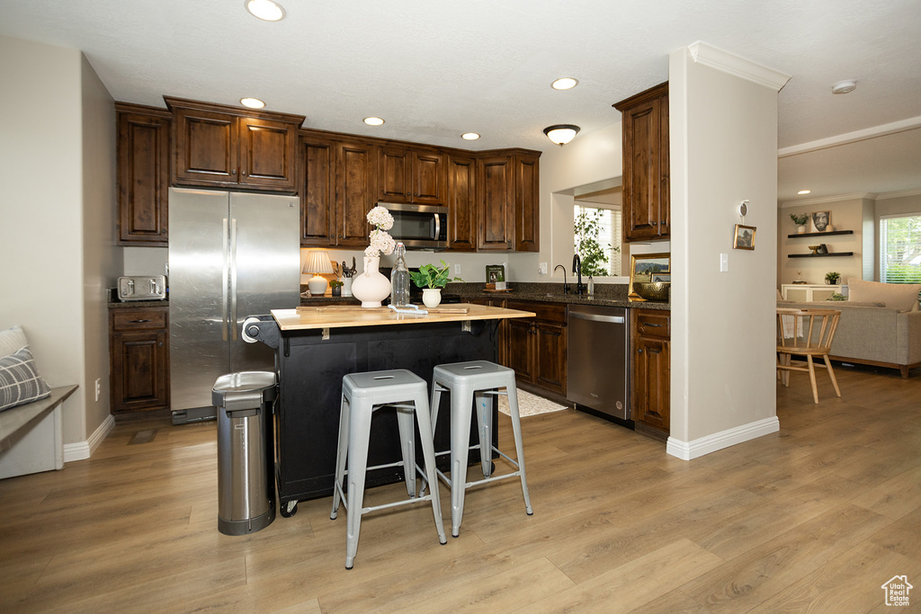 Kitchen with stainless steel appliances, a breakfast bar, recessed lighting, a kitchen island, and light wood finished floors