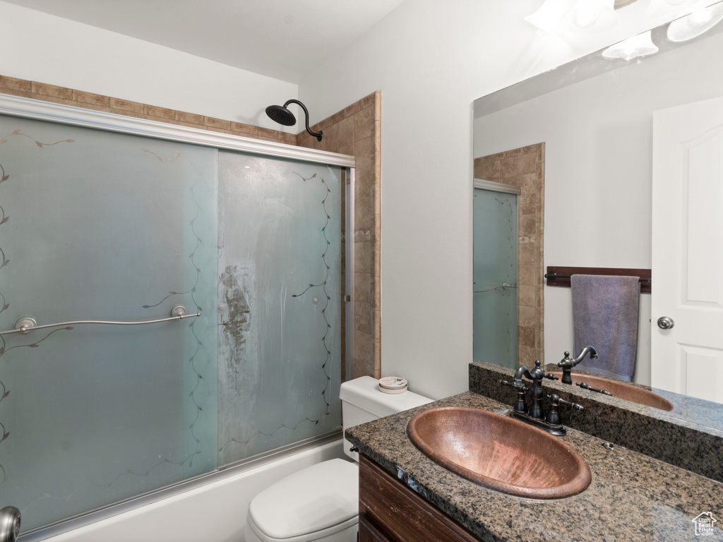 Bathroom featuring bath / shower combo with glass door, vanity, and toilet