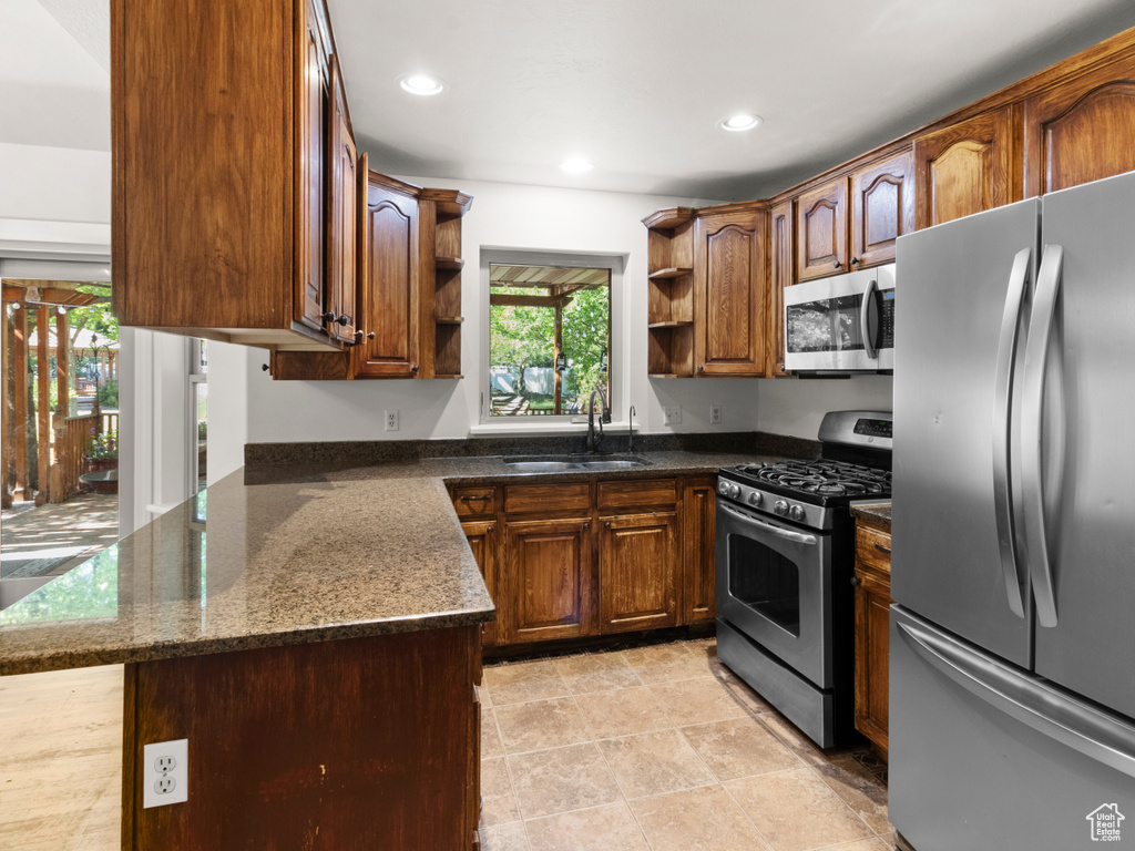 Kitchen with appliances with stainless steel finishes, open shelves, a sink, dark stone countertops, and recessed lighting