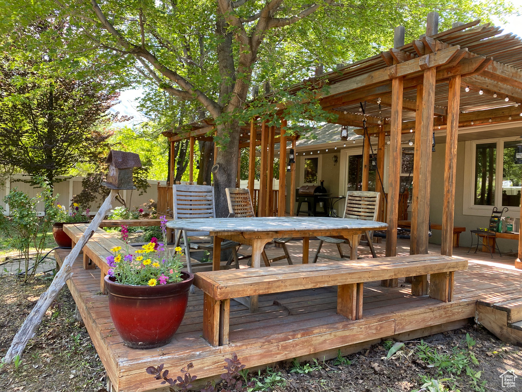 Wooden deck with outdoor dining space, a pergola, and a grill
