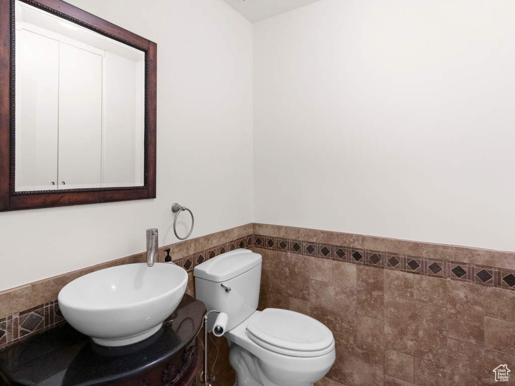 Half bathroom featuring tile walls, a wainscoted wall, and toilet