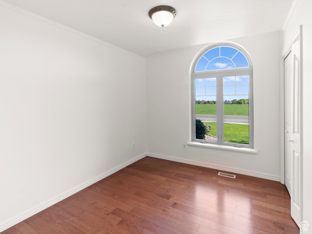 Empty room with wood finished floors, healthy amount of natural light, baseboards, and crown molding