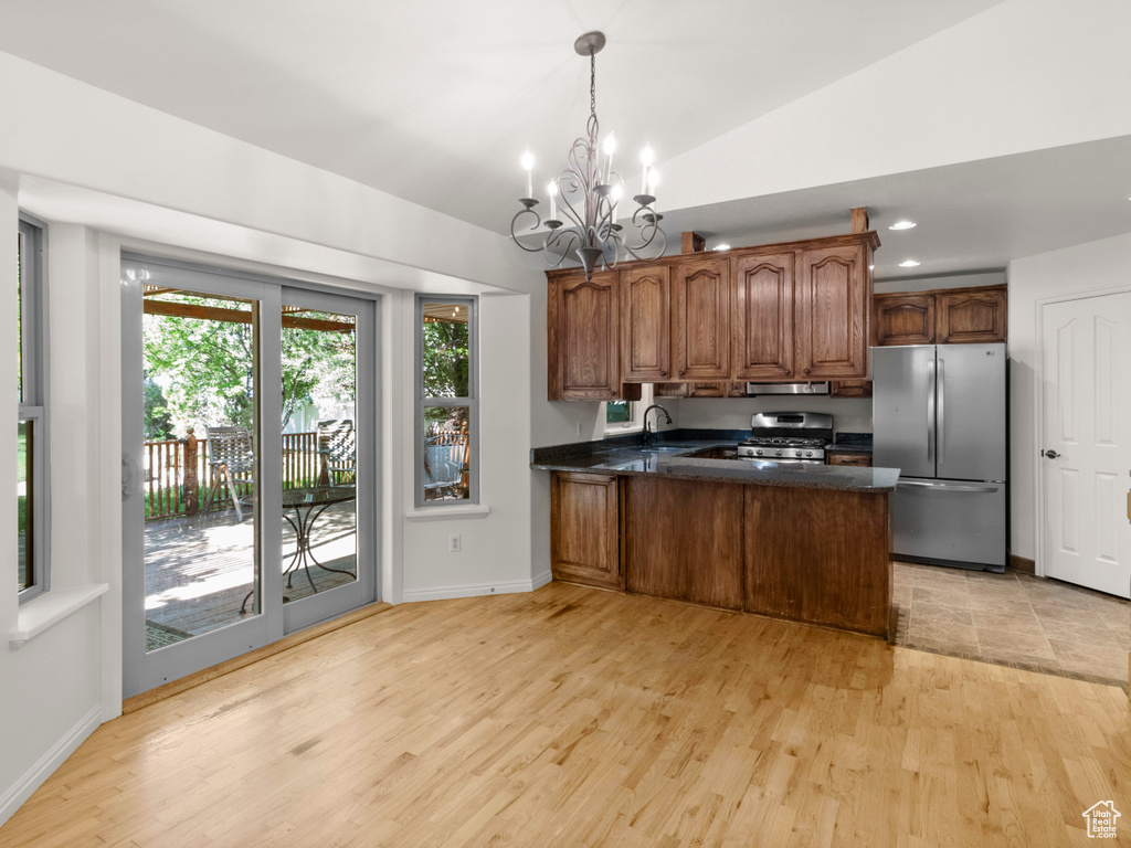 Kitchen with freestanding refrigerator, range with gas stovetop, a chandelier, a peninsula, and light wood-style floors