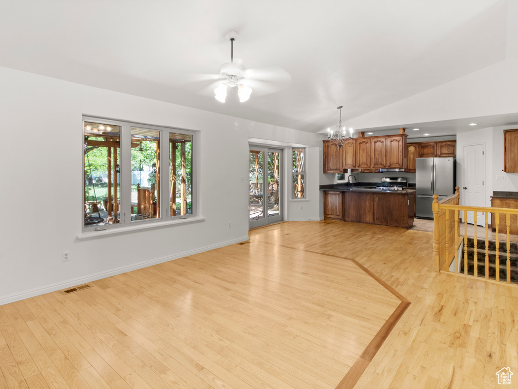 Unfurnished living room featuring a chandelier, light wood-style floors, vaulted ceiling, a ceiling fan, and baseboards