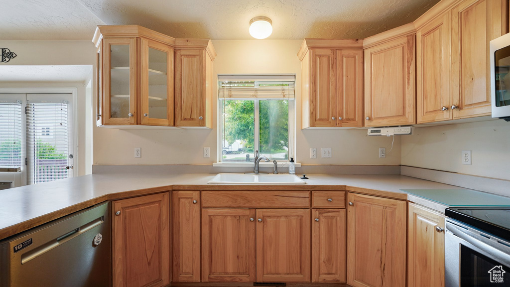 Kitchen featuring stainless steel appliances, a sink, light countertops, and glass insert cabinets