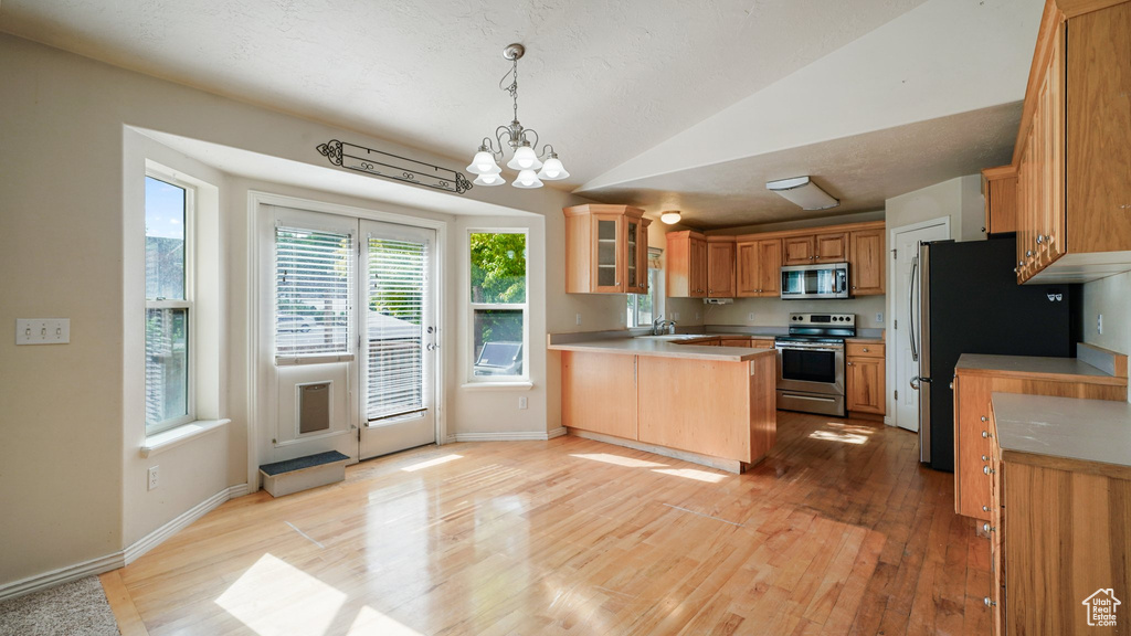 Kitchen featuring stainless steel appliances, a peninsula, a sink, light wood-type flooring, and lofted ceiling