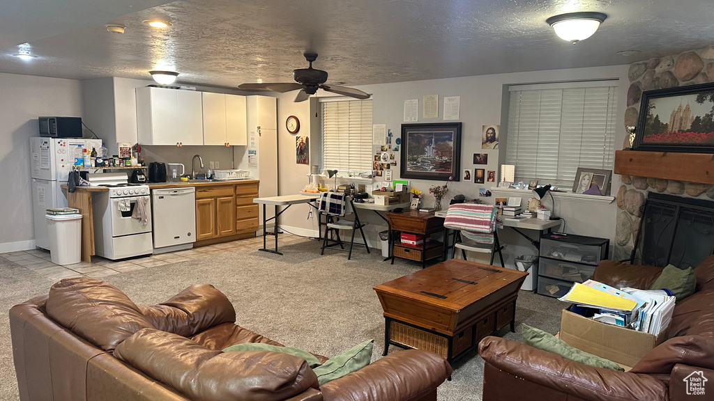 Living area with a ceiling fan, light colored carpet, baseboards, and a stone fireplace
