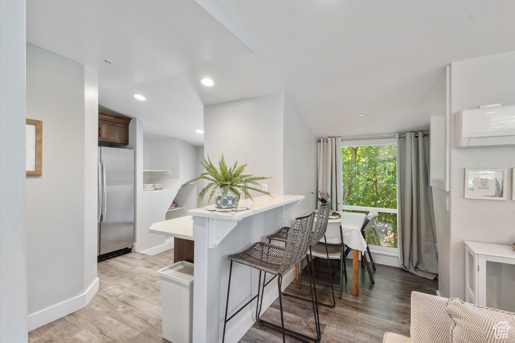 Kitchen with stainless steel refrigerator, light countertops, an AC wall unit, a breakfast bar, and light wood-type flooring