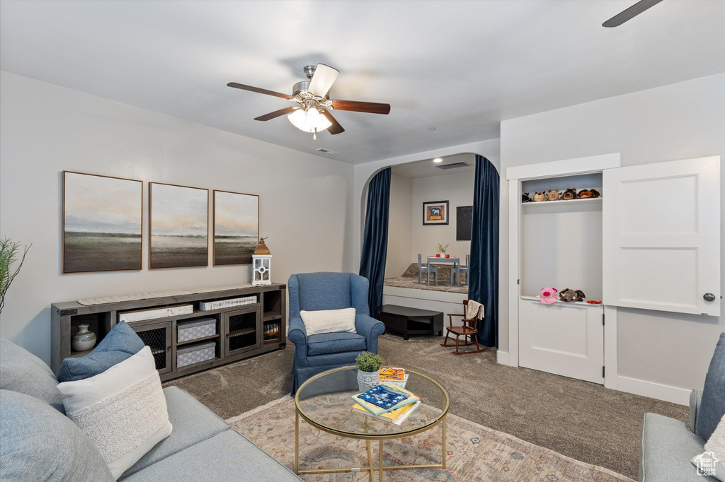 Carpeted living room with ceiling fan and arched walkways