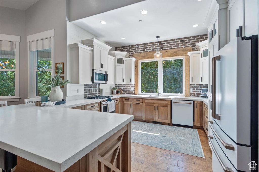 Kitchen with high end appliances, a peninsula, a sink, light countertops, and light wood-style floors