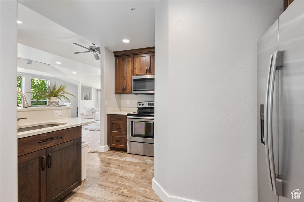 Kitchen featuring stainless steel appliances, a sink, light wood-style flooring, a ceiling fan, and light countertops