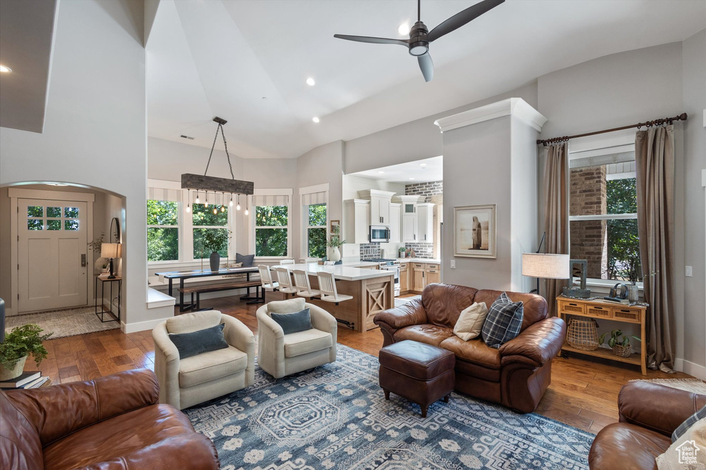 Living area with high vaulted ceiling, arched walkways, ceiling fan, hardwood / wood-style flooring, and recessed lighting