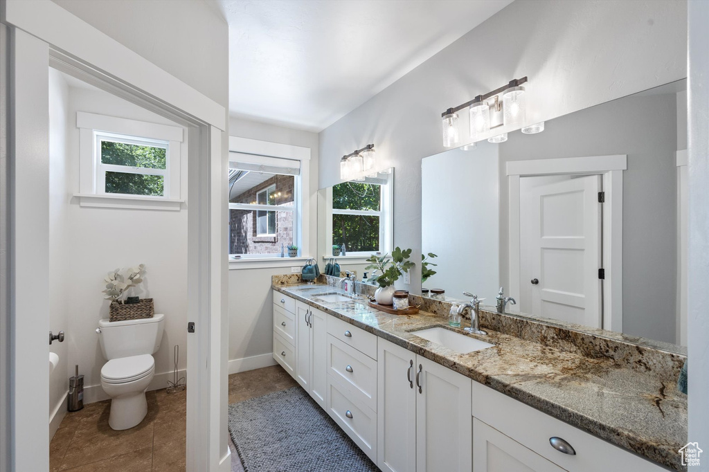 Full bathroom with toilet, double vanity, tile patterned flooring, and baseboards