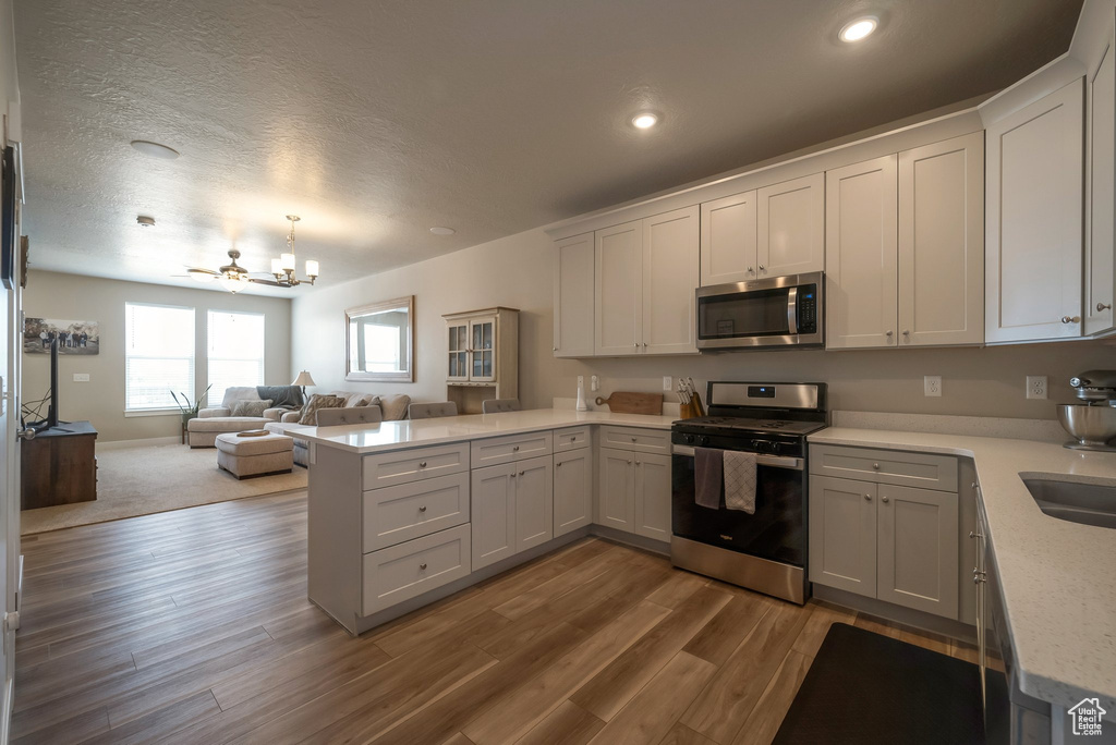 Kitchen featuring stainless steel appliances, a peninsula, open floor plan, a chandelier, and wood finished floors