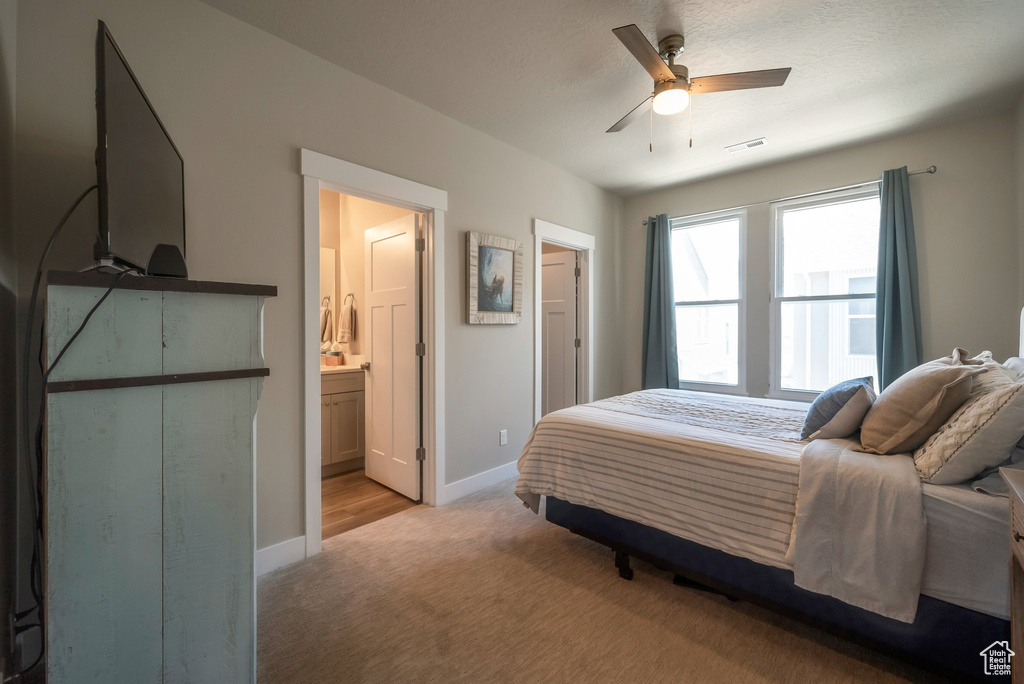 Bedroom with baseboards, light colored carpet, ensuite bath, and a ceiling fan