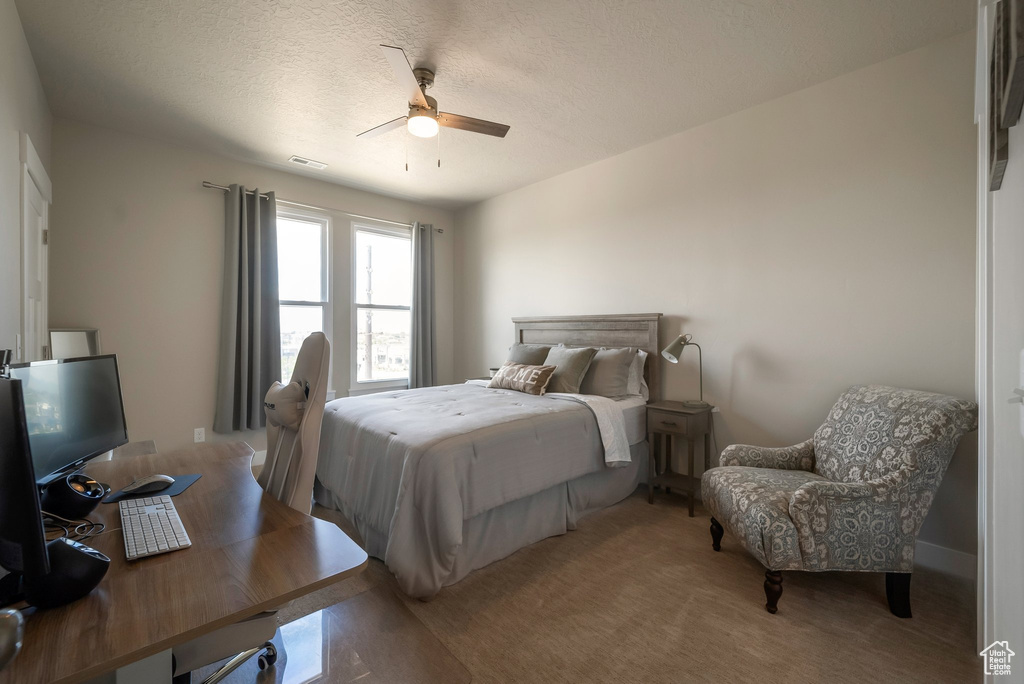Bedroom with an office area, a textured ceiling, a ceiling fan, and light colored carpet
