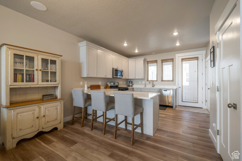 Kitchen with appliances with stainless steel finishes, a peninsula, a breakfast bar, a sink, and wood finished floors