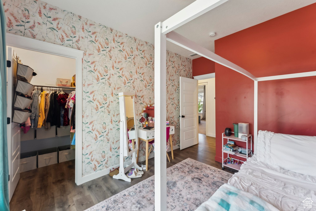 Bedroom featuring wallpapered walls, wood finished floors, baseboards, a closet, and a walk in closet