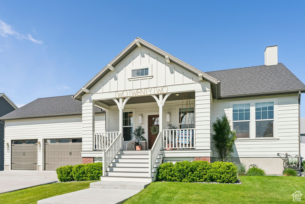 Bungalow-style home with an attached garage, a porch, concrete driveway, a front yard, and a chimney