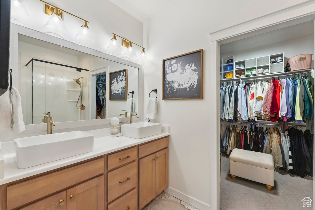 Full bath featuring a walk in closet, a shower stall, double vanity, and baseboards