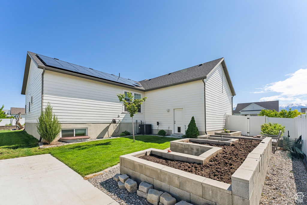 Back of house with a vegetable garden, roof mounted solar panels, and central air condition unit