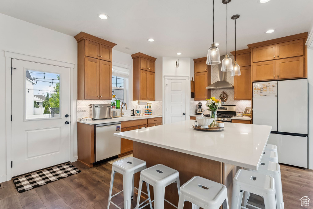 Kitchen featuring stainless steel appliances, wall chimney range hood, a breakfast bar, tasteful backsplash, and recessed lighting