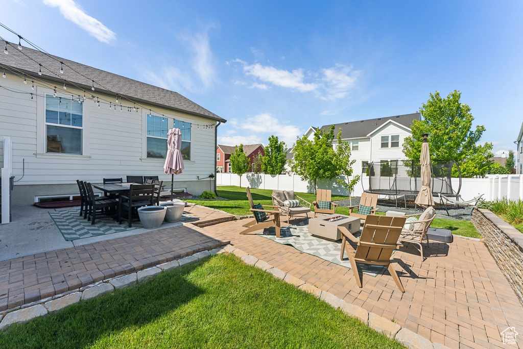 View of patio featuring a trampoline, a fire pit, and outdoor dining space