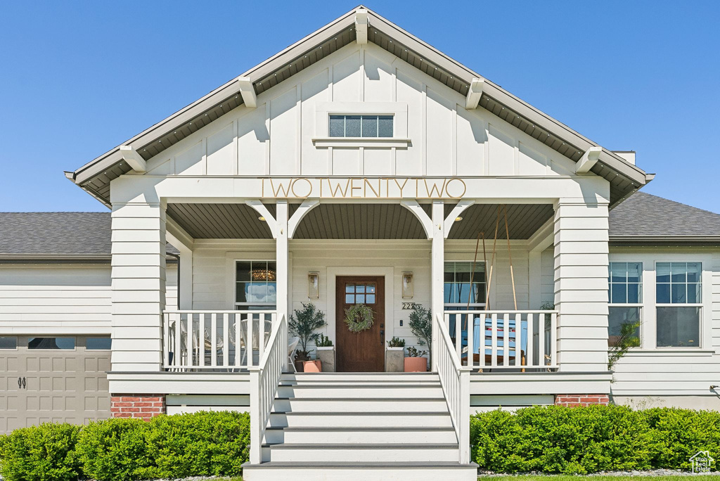View of front of house featuring covered porch, roof with shingles, board and batten siding, and stairway
