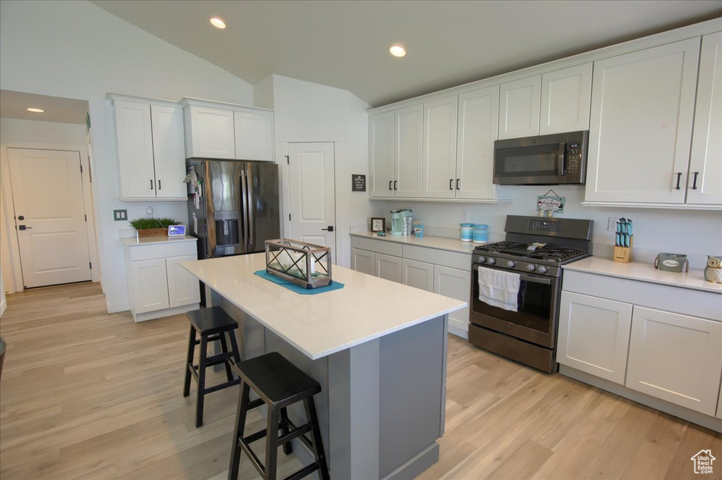 Kitchen with stainless steel appliances, a kitchen bar, vaulted ceiling, light wood-type flooring, and light countertops