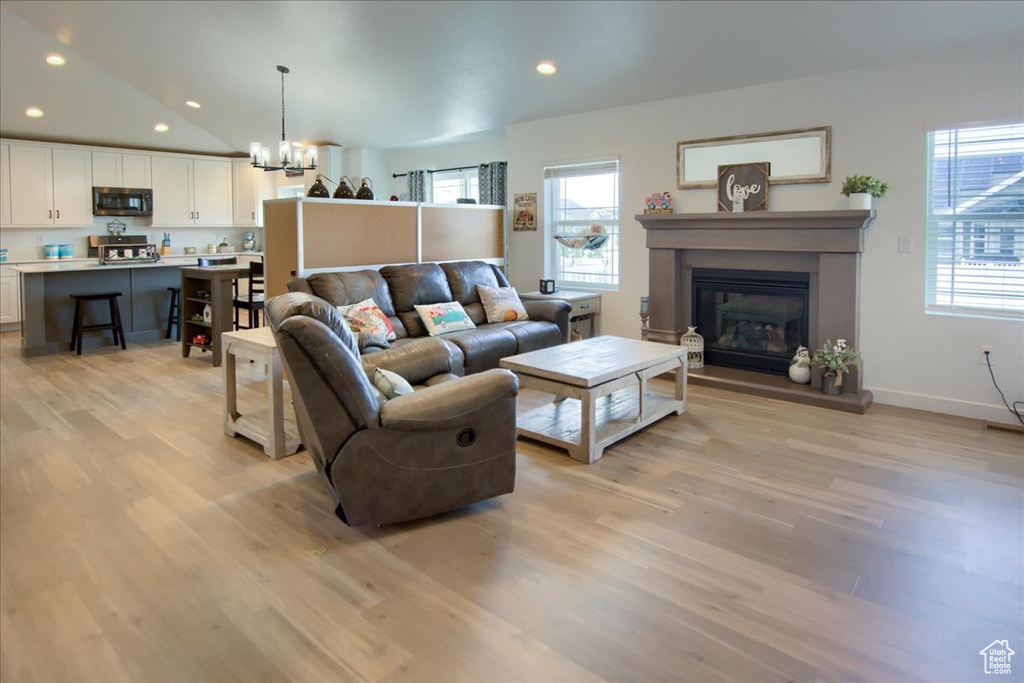 Living area with light wood-type flooring, a chandelier, a glass covered fireplace, recessed lighting, and baseboards