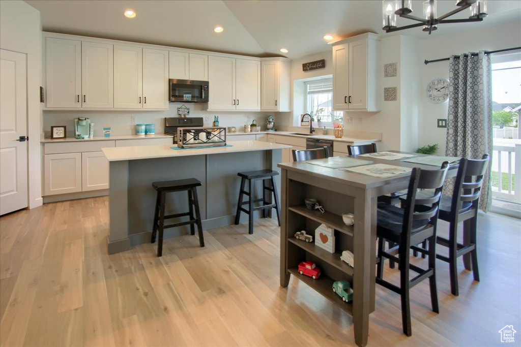 Kitchen with stainless steel appliances, white cabinets, a kitchen island, light countertops, and lofted ceiling