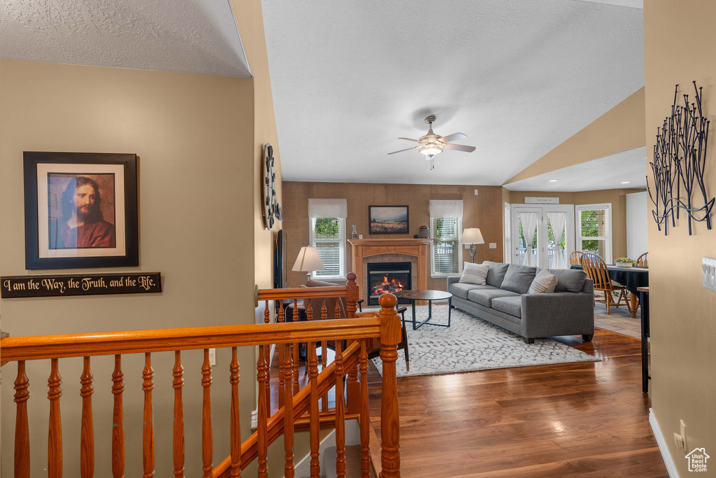 Living room with ceiling fan, a glass covered fireplace, healthy amount of natural light, wood finished floors, and a textured ceiling