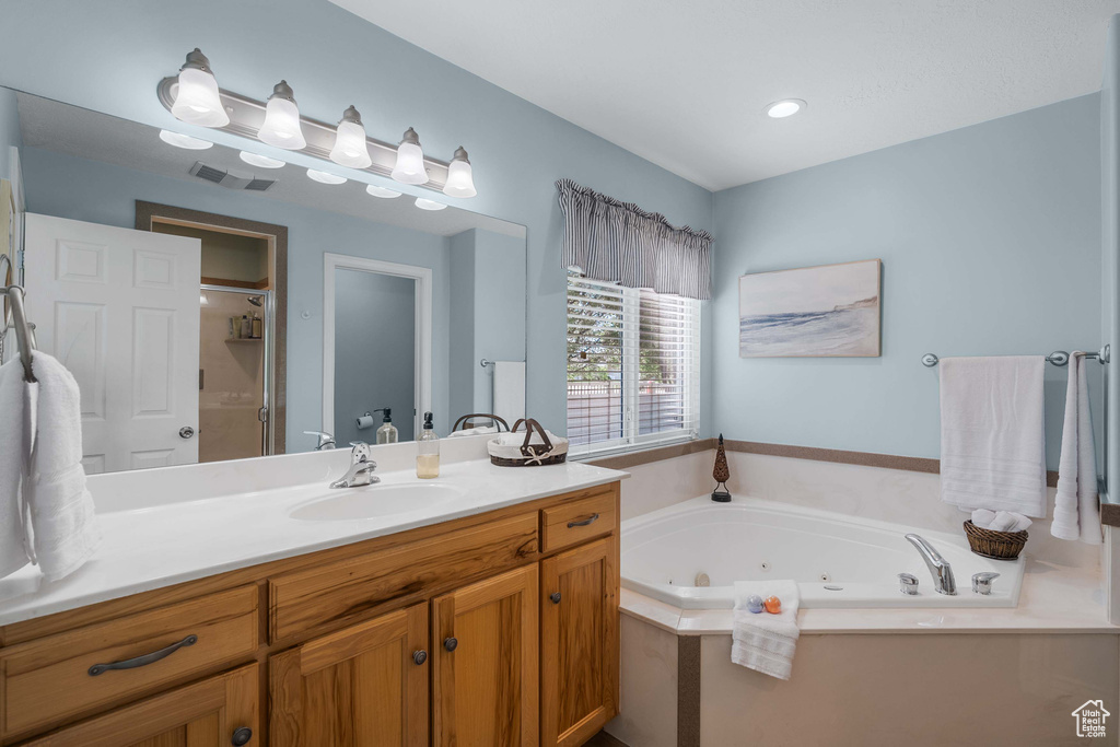 Bathroom featuring vanity, a jetted tub, and a shower
