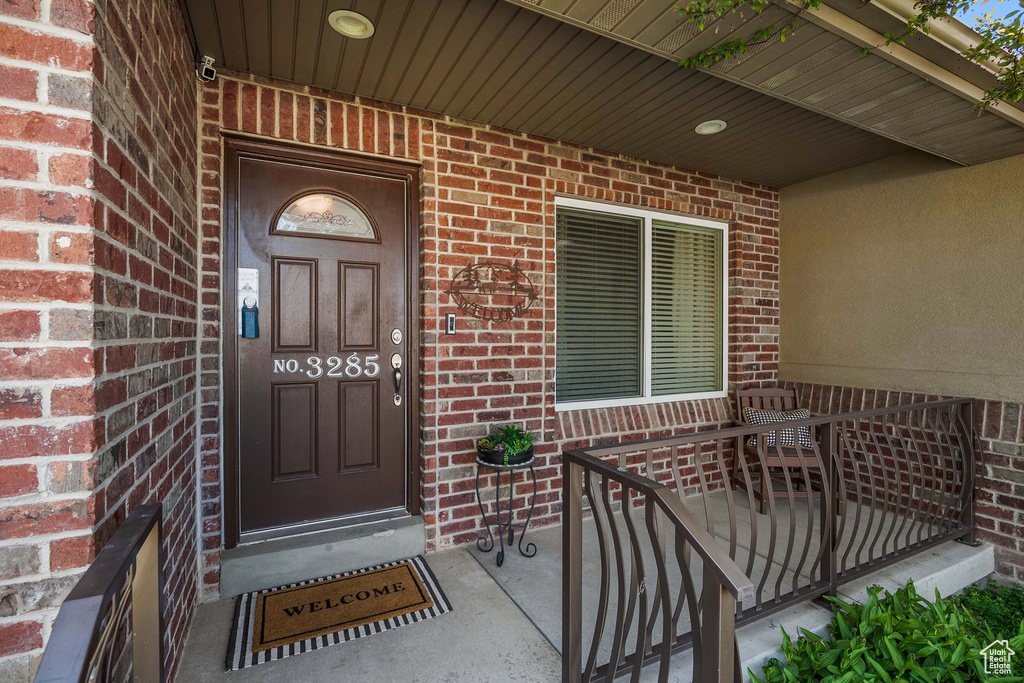 Entrance to property featuring brick siding, a porch, and a security system