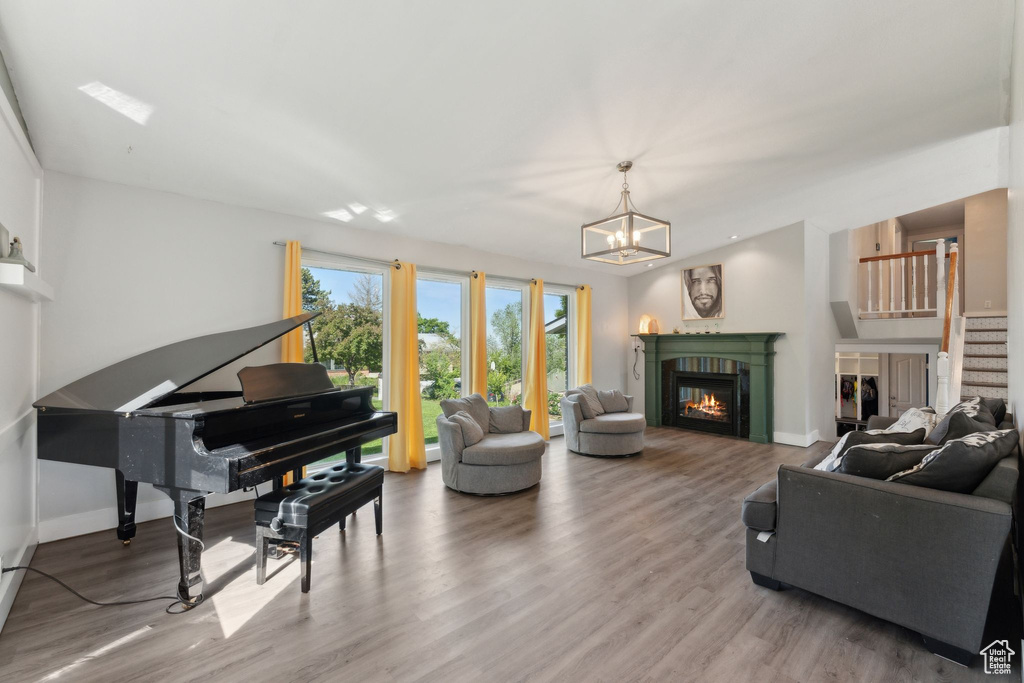 Living room with wood finished floors, a glass covered fireplace, stairway, and a chandelier