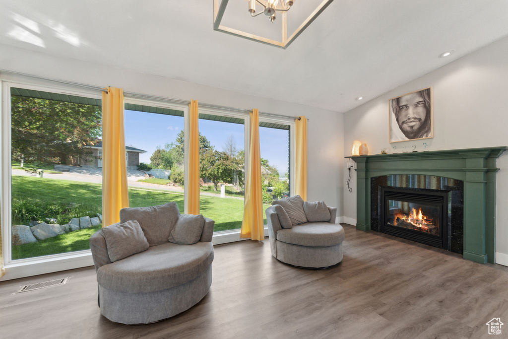 Living area featuring vaulted ceiling, a glass covered fireplace, wood finished floors, a chandelier, and recessed lighting