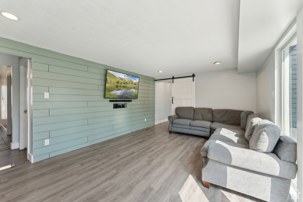Living area featuring a barn door, wood walls, wood finished floors, recessed lighting, and baseboards