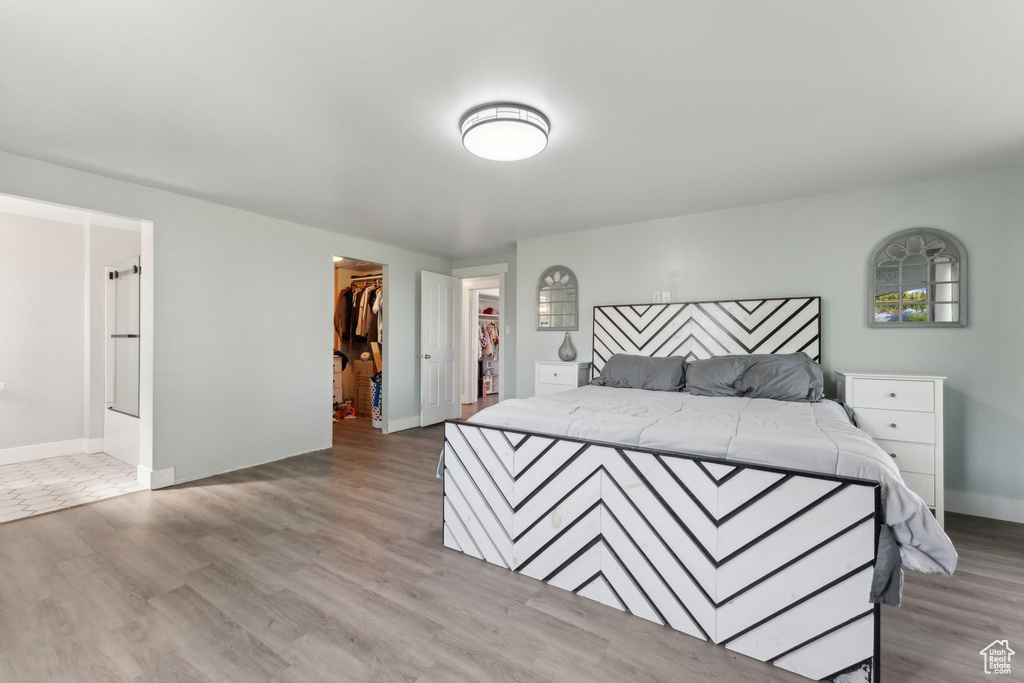Bedroom with a spacious closet, light wood-style flooring, baseboards, and a closet