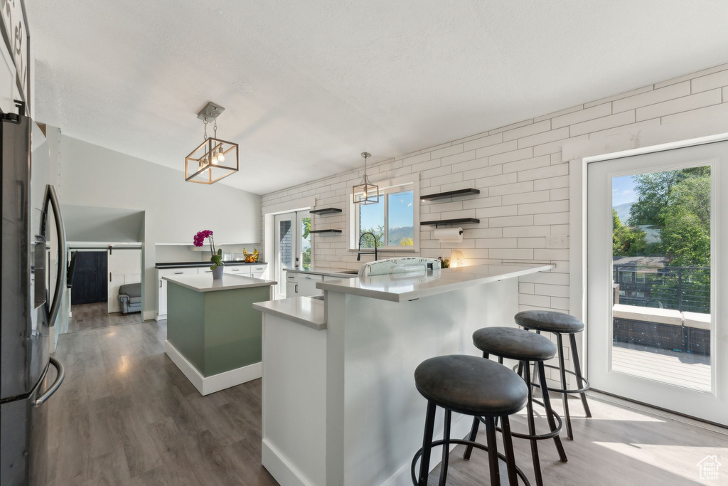 Kitchen with stainless steel fridge, dark wood-style flooring, a center island, a chandelier, and a kitchen bar