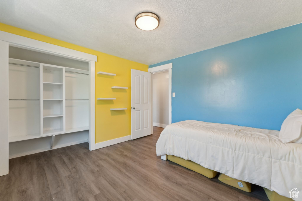 Bedroom featuring baseboards, wood finished floors, a textured ceiling, and a closet