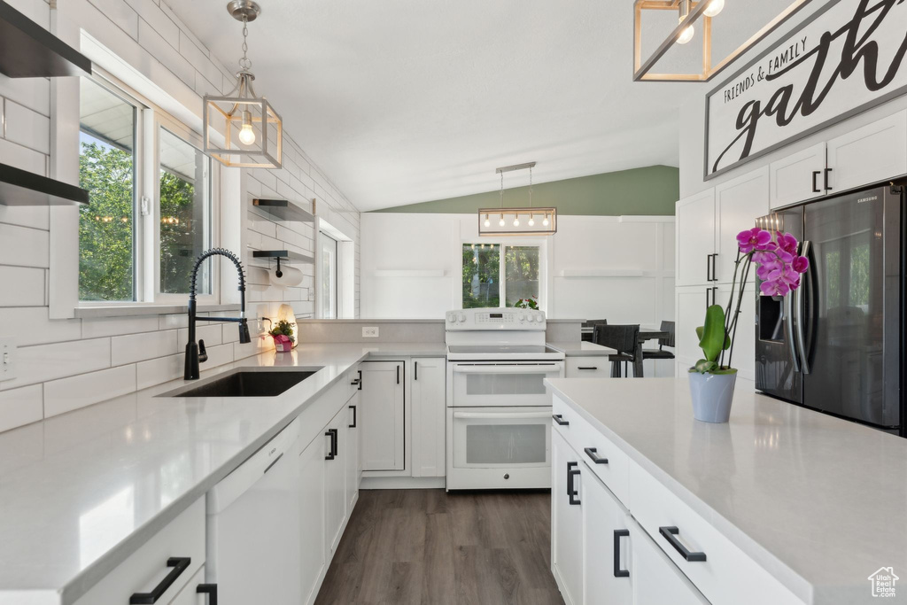 Kitchen featuring white appliances, a sink, lofted ceiling, healthy amount of natural light, and white cabinetry