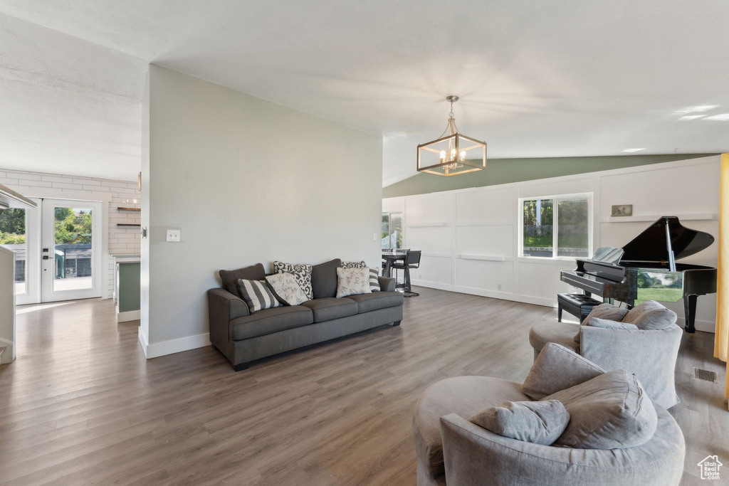 Living area with vaulted ceiling, a chandelier, wood finished floors, plenty of natural light, and baseboards