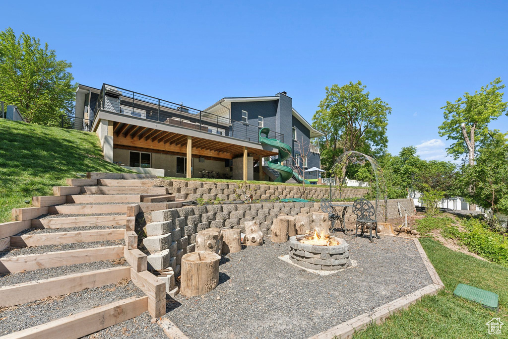 Back of property featuring a wooden deck, an outdoor fire pit, stairway, a lawn, and a patio
