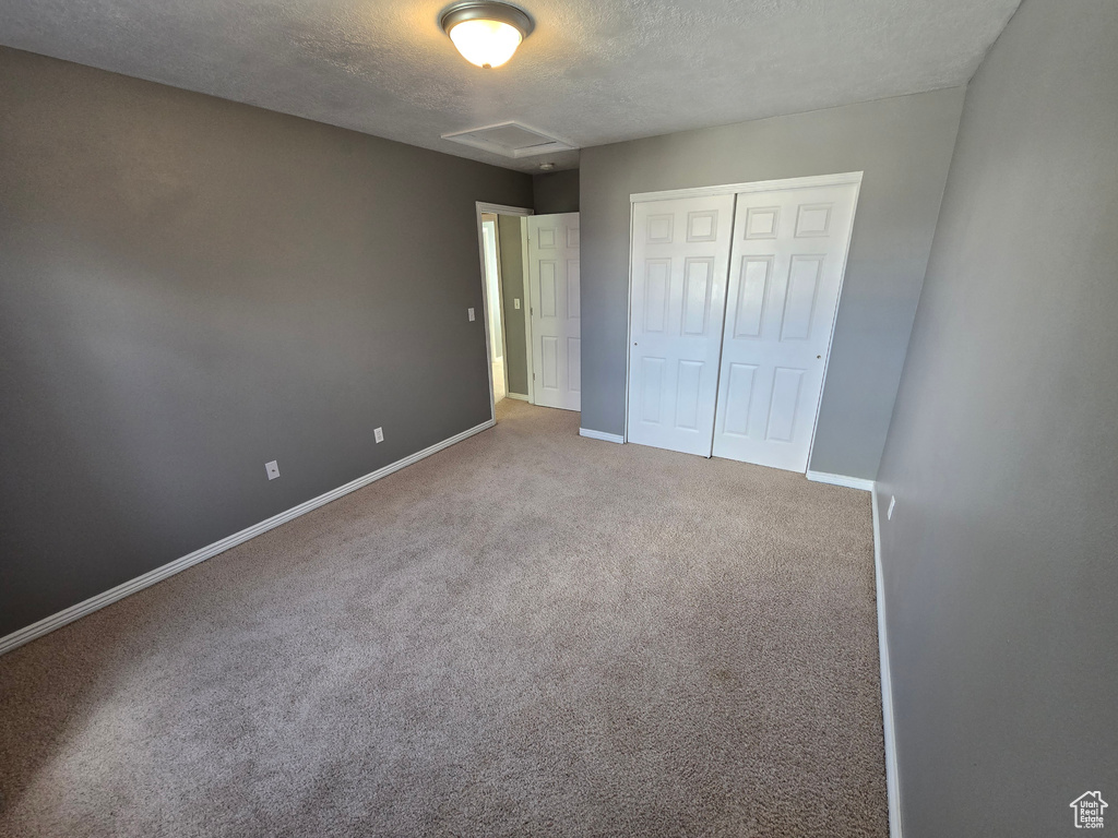 Unfurnished bedroom featuring a textured ceiling, baseboards, carpet floors, a closet, and attic access