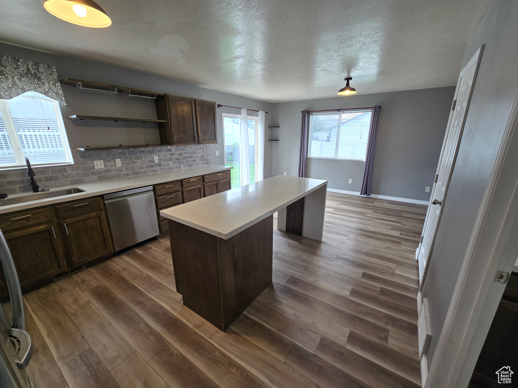 Kitchen with dishwasher, a sink, a center island, light countertops, and tasteful backsplash