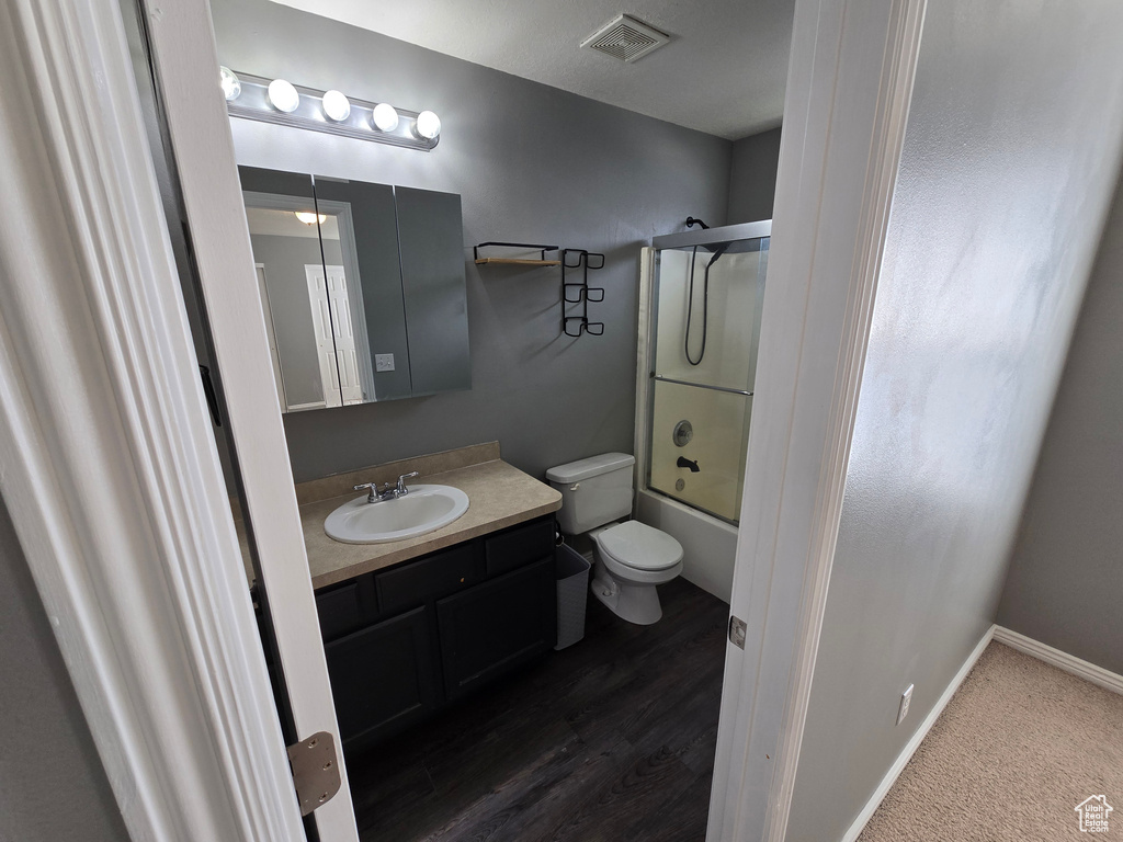 Bathroom with toilet, vanity, combined bath / shower with glass door, and baseboards