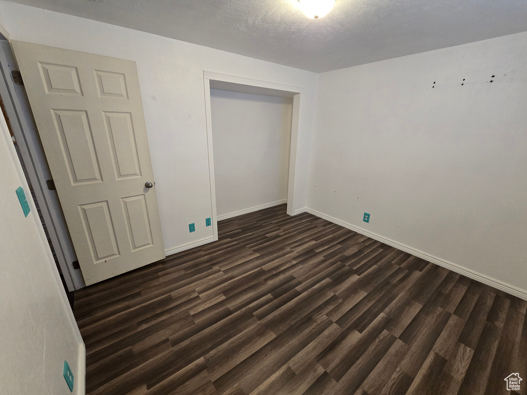 Unfurnished bedroom with dark wood-style floors, a closet, and baseboards