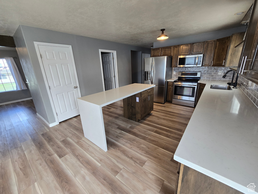 Kitchen with stainless steel appliances, a sink, a kitchen island, light countertops, and tasteful backsplash